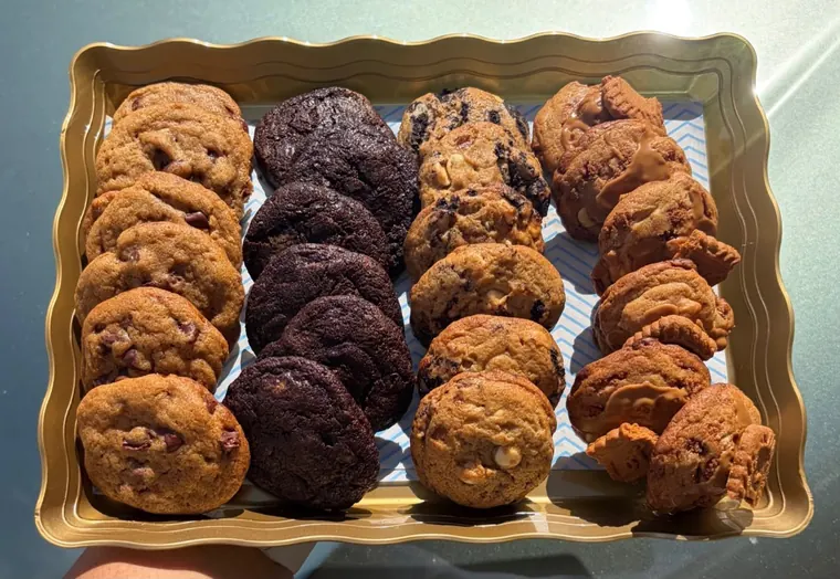 A scalloped gold tray holding rows of chocolate chip, double chocolate, cookies and cream and Biscoff cookies