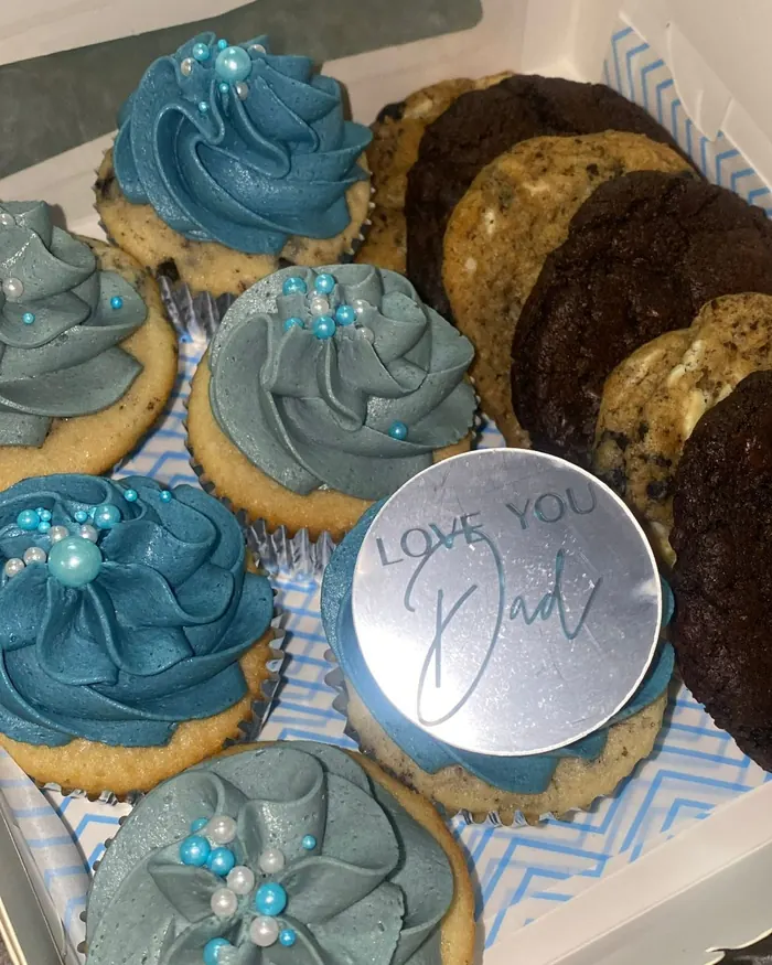 Cupcakes piped in shades of blue with pearl sprinkles and a silver Love You Dad topper, boxed with cookies